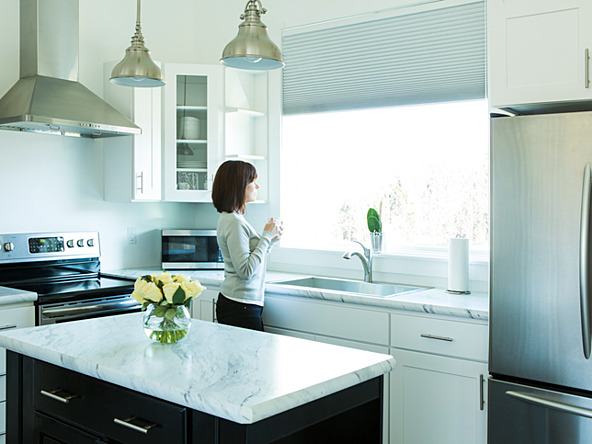 woman drinking coffee in modern, sterile kitchen while looking out window